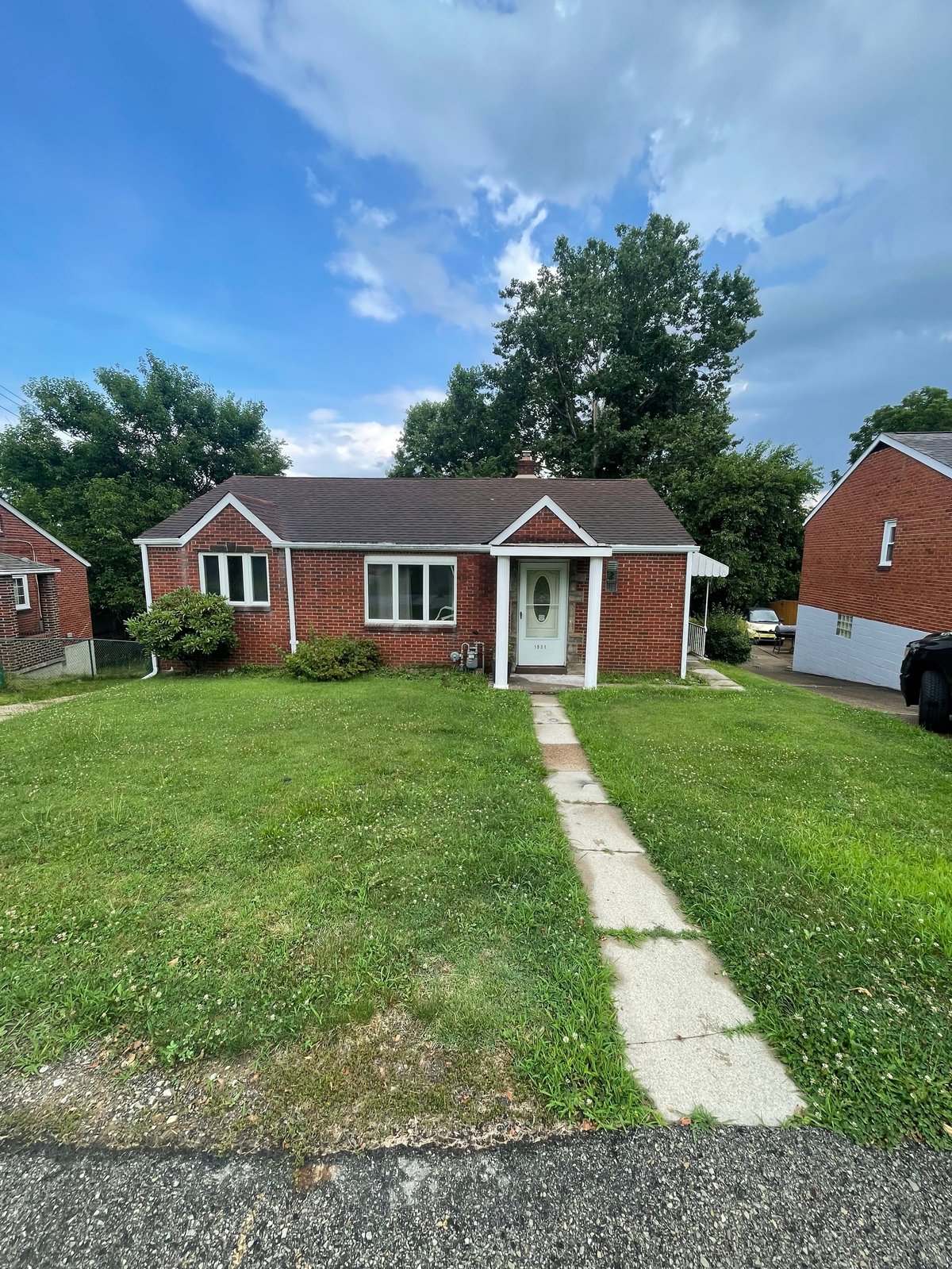 Red brick single-story residential home with white trim, front porch, and manicured lawn with concrete walkway